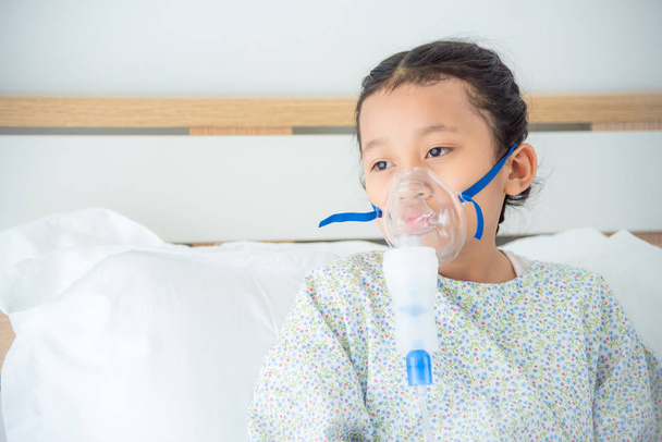 sick girl sitting on bed with oxygen mask  - 写真・画像