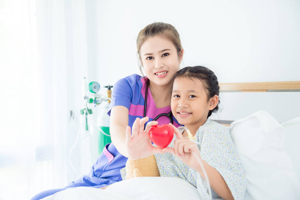 κορίτσι ασθενής και γυναίκα γιατρός κρατώντας κόκκινο μπάλα καρδιά και χαμόγελο - Φωτογραφία, εικόνα