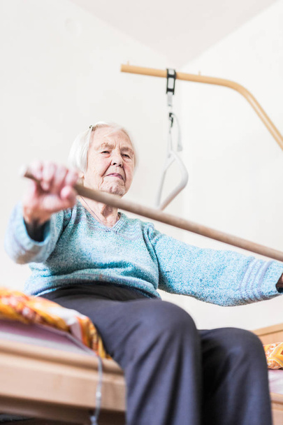 Personnes âgées 96 ans femme exerçant avec un bâton assis sur sa mauvaise. - Photo, image