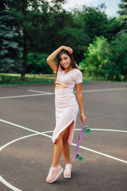 Portrait of a smiling charming brunette female holding her skateboard on a basketball court. - Foto, Imagem