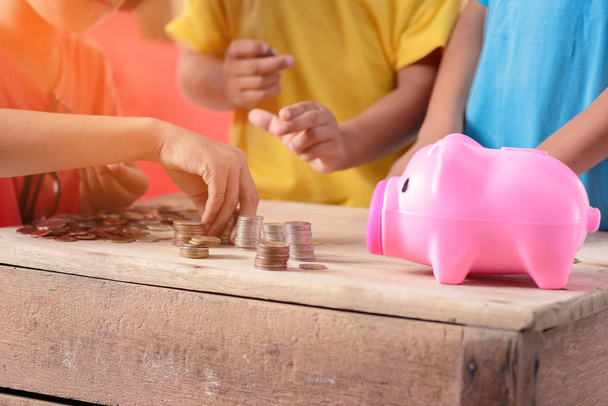 Hands of children are helping putting coins into piggy bank on w - Photo, Image