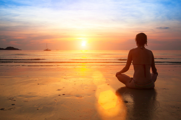 Frau praktiziert Yoga am Meeresstrand bei Sonnenuntergang. - Foto, Bild