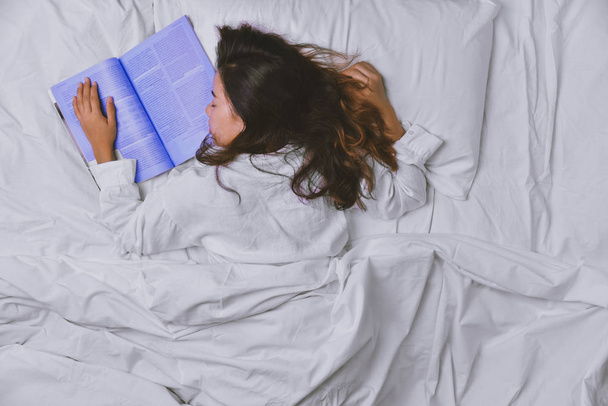 ベッドで寝ている若い女性。若い女性のトップビューのベッドでよく寝て横たわっ。ベッドで本を読んで寝ている少女。リラックス、リラックス、睡眠、教育、読書、本、楽しみ、幸せ、深い眠り. - 写真・画像