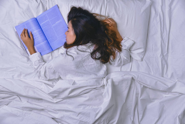 Młoda kobieta śpiąca w łóżku. Widok na leżącą młodą kobietę śpiącą dobrze w łóżku. Dziewczyna, która czytała książkę w łóżku i spała. spanie relaks, relaks, spanie, edukacja, czytanie; książka, radość, szczęśliwy, głęboki sen. - Zdjęcie, obraz