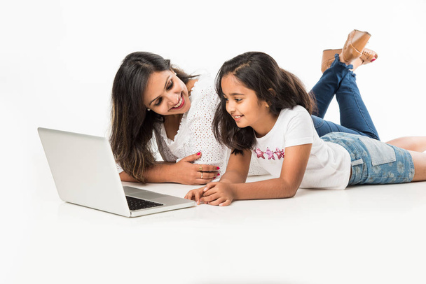Indiase moeder en dochter liggen op de vloer met boek, laptop of tablet computer studeren of het lezen van verhaal of het spelen van games - Foto, afbeelding