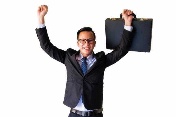 Azjatycki biznesmen trzymając walizka i podnieść ręce uśmiechniętą twarzą wyizolowaną na białym tle. Zadowolony z promocji przez sukces projektu. - Zdjęcie, obraz