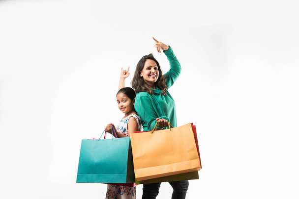 Индийско-азиатская мать дочь делает покупки и держит цветные бумажные пакеты. стоять изолированно над белым фоном
 - Фото, изображение