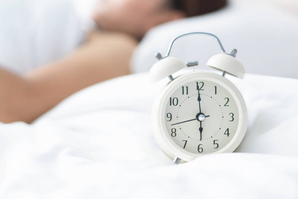 Acercamiento mujer durmiendo en la cama y la mano sosteniendo la alarma en el reloj, hora de despertar
 - Foto, Imagen