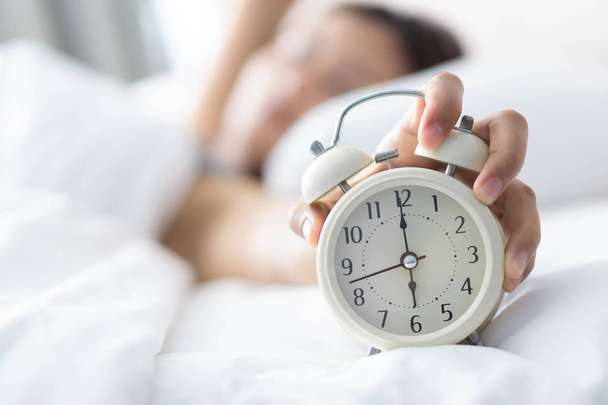 Lähikuva nainen nukkuu sängyssä ja käsi pitäen herätys kello, aika herätä
 - Valokuva, kuva