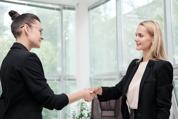 Two beautiful young women in business suits shake hands and smile. Hiring a job. Signing the agreement. Women at work. - Фото, изображение