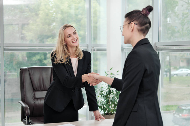 Two beautiful young women in business suits shake hands and smile. Hiring a job. Signing the agreement. Women at work. - Foto, Imagem