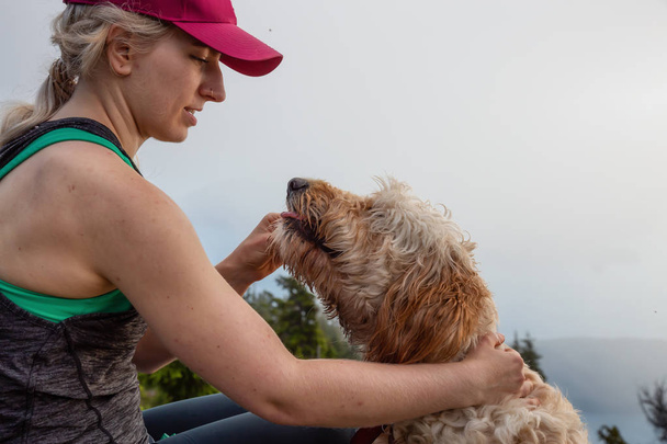 Seikkaileva tyttö patikoi koiran kanssa tarpeettoman vuoren huipulla aurinkoisena ja pilvisenä kesäpäivänä. Kaupungissa West Vancouver, British Columbia, Kanada
. - Valokuva, kuva