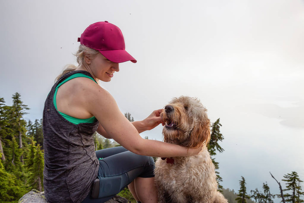Adventurous Girl is hiking with a dog on top of Unnecessary Mountain during a sunny and cloudy summer day. Located in West Vancouver, British Columbia, Canada. - Zdjęcie, obraz