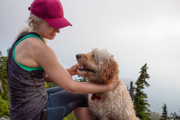Adventurous Girl is hiking with a dog on top of Unnecessary Mountain during a sunny and cloudy summer day. Located in West Vancouver, British Columbia, Canada. - Фото, изображение