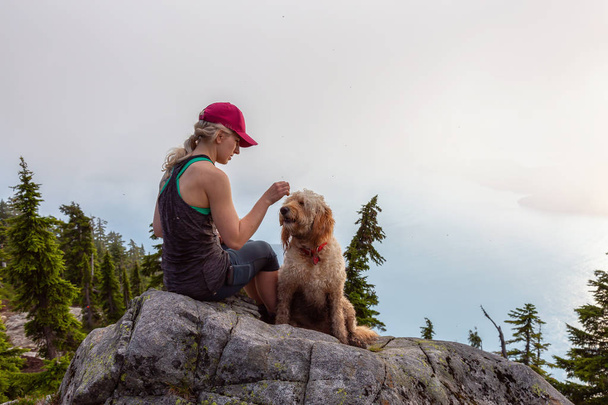 Adventurous Girl is hiking with a dog on top of Unnecessary Mountain during a sunny and cloudy summer day. Located in West Vancouver, British Columbia, Canada. - Φωτογραφία, εικόνα