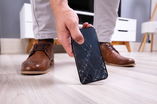 Man's Hand Picking Up Mobile Phone With Broken Screen - Foto, immagini