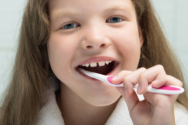 little girl in a white robe smiling brushes her teeth, close-up - Foto, Imagen