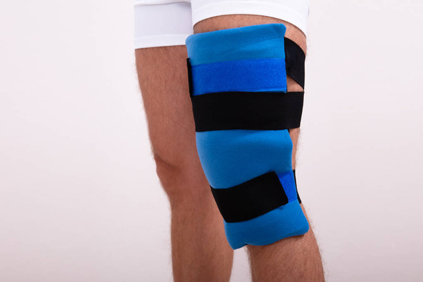 Close-up Of A Man With Blue Knee Ice Pack Against White Backdrop - Foto, Imagen