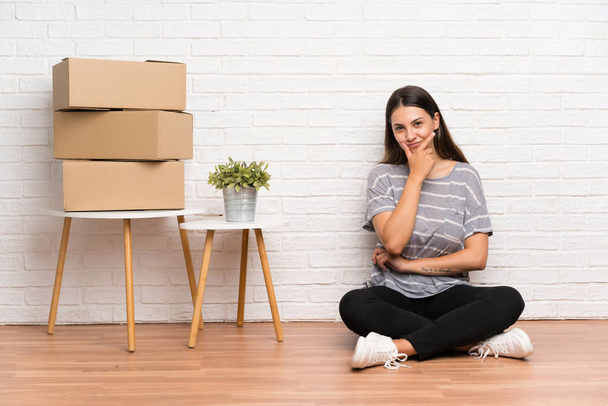 Young woman moving in new home among boxes thinking an idea - Photo, Image