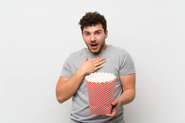 Mann mit lockigem Haar über isolierter Wand mit einer Schüssel Popcorn - Foto, Bild