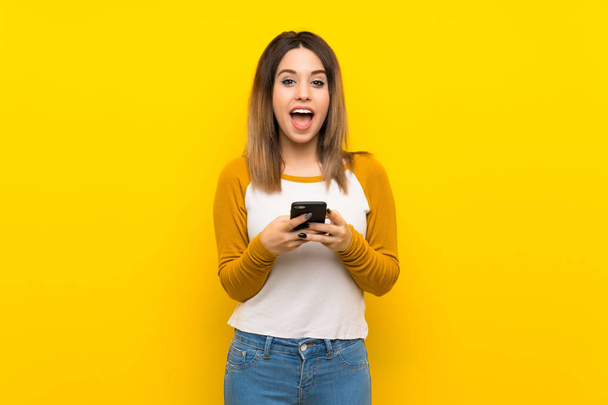 Kaunis nuori nainen yli eristetty keltainen seinä yllättynyt ja lähettää viestin
 - Valokuva, kuva
