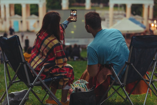 couple taking selfie in city park while watching movie in open air cinema - Photo, Image