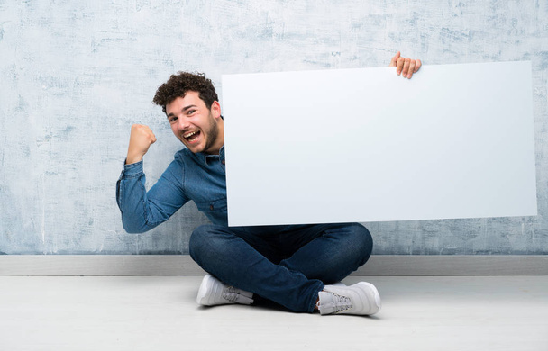 Genç adam bir kavram eklemek için boş bir beyaz pankart tutarak katta oturan - Fotoğraf, Görsel
