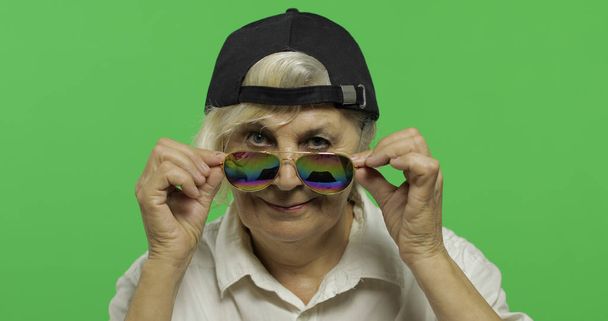 Μια ηλικιωμένη γυναίκα με γυαλιά ηλίου και χαμόγελα από καπέλο. Η γριά γιαγιά. Πλήκτρο αποχρώσεων - Φωτογραφία, εικόνα