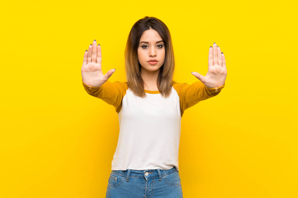Mooie jonge vrouw over geïsoleerde gele muur maken stop gebaar en teleurgesteld - Foto, afbeelding