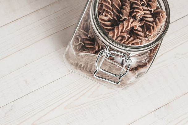 On a white board rustic table a glass jar with Italian pasta - Zdjęcie, obraz