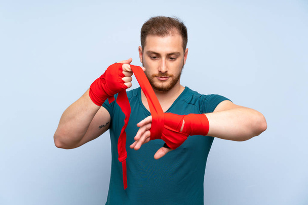 Blonde sport man over blue wall in boxing bandages - Photo, Image