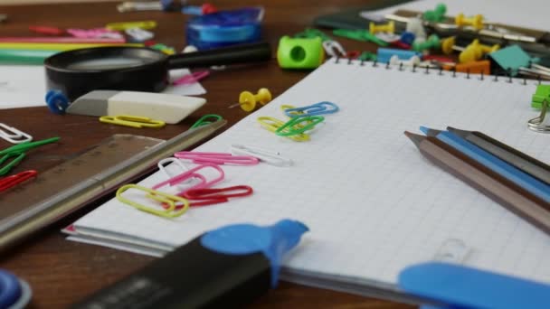 Πολύχρωμα μολύβια, κλιπ χαρτιού και σημειωματάριο σε καφέ ξύλινο γραφείο - Πλάνα, βίντεο
