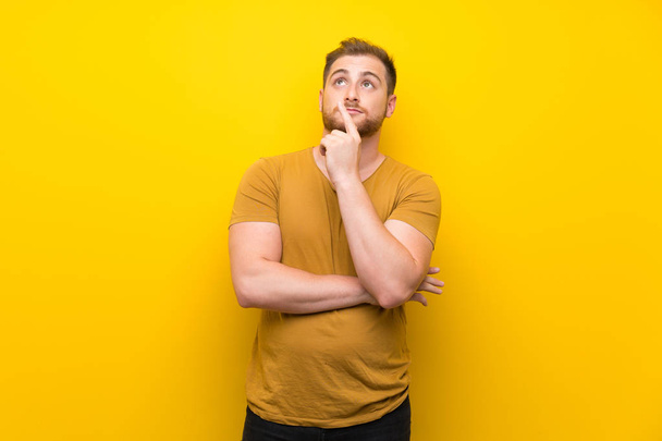 Hombre rubio sobre aislada pared amarilla pensando en una idea apuntando con el dedo hacia arriba
 - Foto, imagen