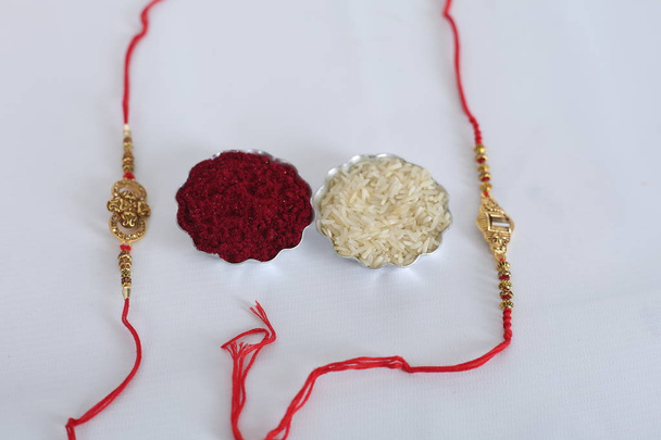 インドの祭り:エレガントなラキ、米粒、クムクムとラクシャバンダンの背景。兄弟姉妹間の愛の象徴である伝統的なインドの手首バンド. - 写真・画像