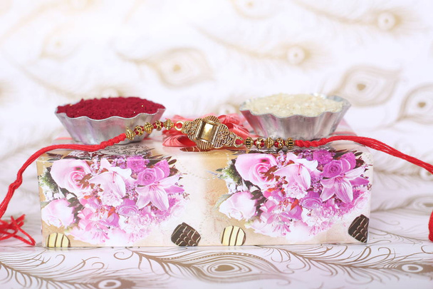 Indisches Festival: Raksha Bandhan Hintergrund mit einem eleganten Rakhi, Reiskörner und Kumkum. Ein traditionelles indisches Armband, das ein Symbol der Liebe zwischen Brüdern und Schwestern ist. - Foto, Bild
