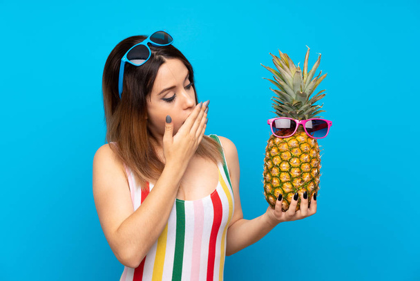 Young woman in summer holidays over blue background holding a pineapple with sunglasses - Foto, Bild