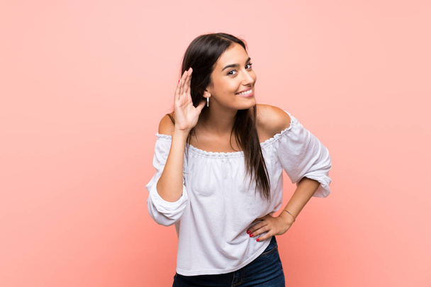 Young woman over isolated pink background listening to something by putting hand on the ear - Fotoğraf, Görsel
