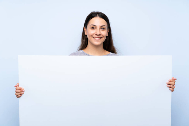Mladá brunetka na izolovaném modrém pozadí s prázdným bílým placením pro vložení konceptu - Fotografie, Obrázek