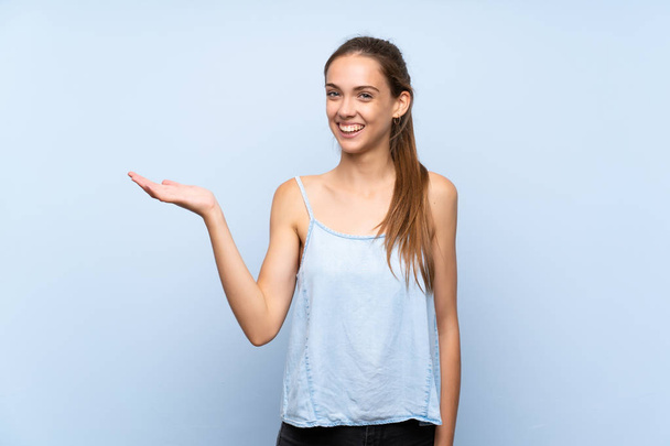 Jonge vrouw over geïsoleerde blauwe achtergrond houden copyspace imaginaire op de palm om een advertentie in te voegen - Foto, afbeelding