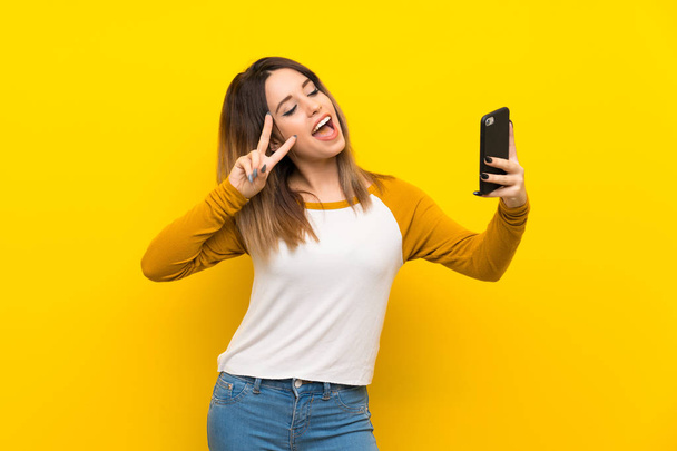 Pretty young woman over isolated yellow wall making a selfie - Fotografie, Obrázek