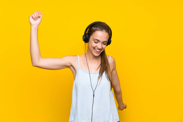 Щаслива молода жінка слухає музику над ізольованою жовтою стіною
 - Фото, зображення