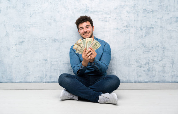 Young man sitting on the floor taking a lot of money - Fotoğraf, Görsel