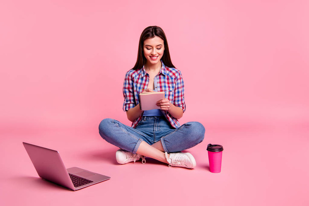 フルレングスボディサイズ写真美しい彼女彼女の女性が座る床のノートブックは、手を保持し、主催者は、カジュアルなチェッカーチェックのシャツジーンズデニム孤立したピンクの背景を着用する便利な大学のウェブサイトを着用します - 写真・画像