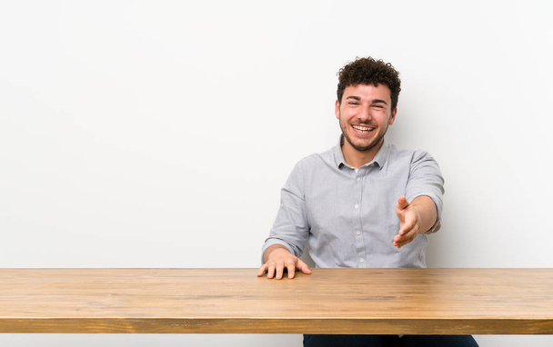 Jonge man met een tafel handen schudden voor het sluiten van een goede deal - Foto, afbeelding