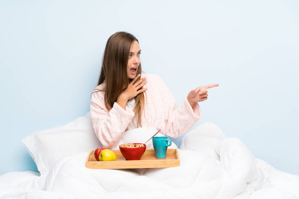 Jeune femme en robe de chambre avec petit déjeuner pointant du doigt sur le côté
 - Photo, image