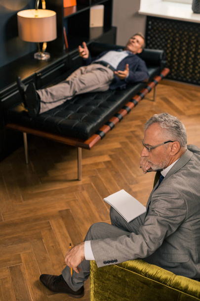 Thoughtful serious psychotherapist sitting next to his patient - Zdjęcie, obraz