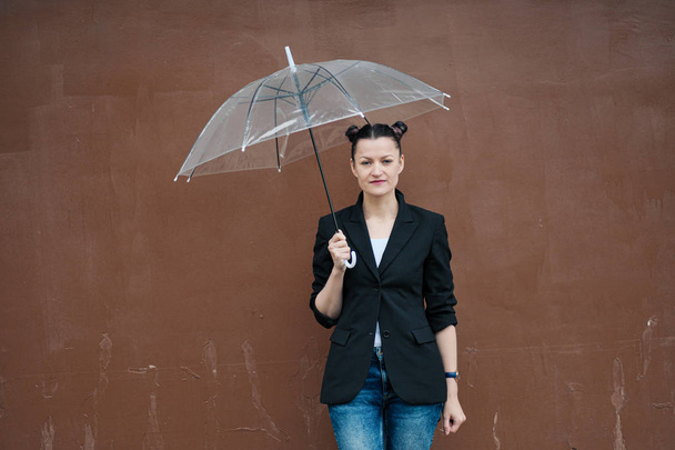 Young attractive woman in black jacket and blue jeans posing outdoor against background of building. - Valokuva, kuva