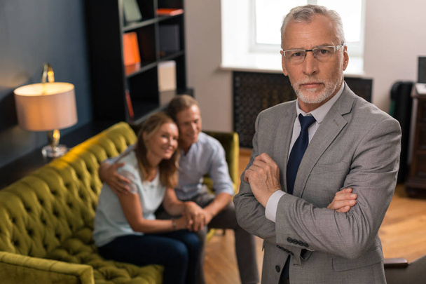 Serious grey-haired professional psychotherapist standing in his office - Foto, afbeelding