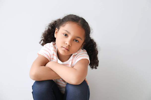 Porträt eines traurigen kleinen afrikanisch-amerikanischen Mädchens auf hellem Hintergrund - Foto, Bild