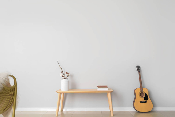 Mesa con guitarra cerca de pared de luz en la habitación
 - Foto, imagen